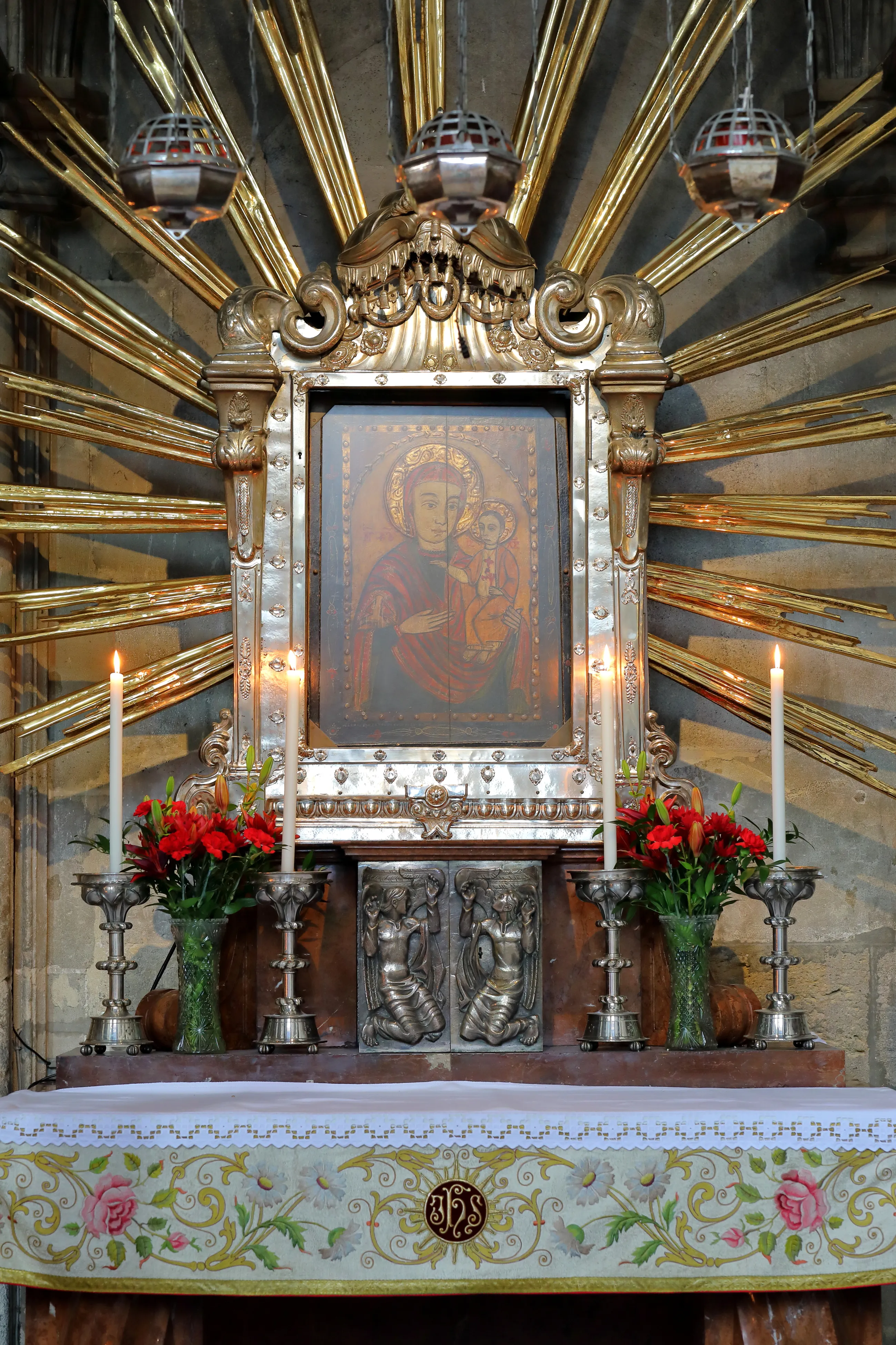 Religieus altaar met een centrale icoon van de Maagd Maria met Kind, omringd door rode bloemen, kaarsen en een gouden stralende achtergrond