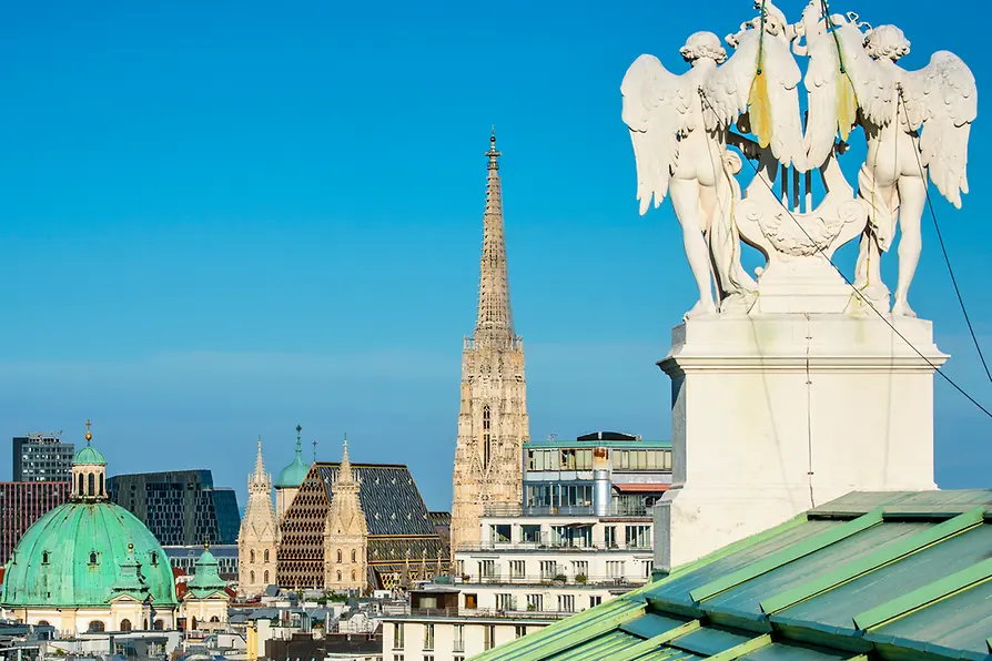 St. Stephen's Cathedral spire and angel sculpture with city rooftops and a clear blue sky