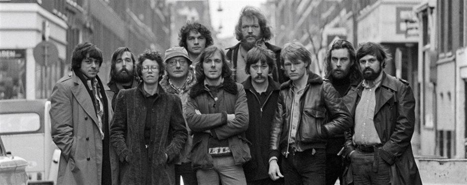 Group of twelve people standing on an Amsterdam street, black and white historical photograph with buildings and a vehicle in background