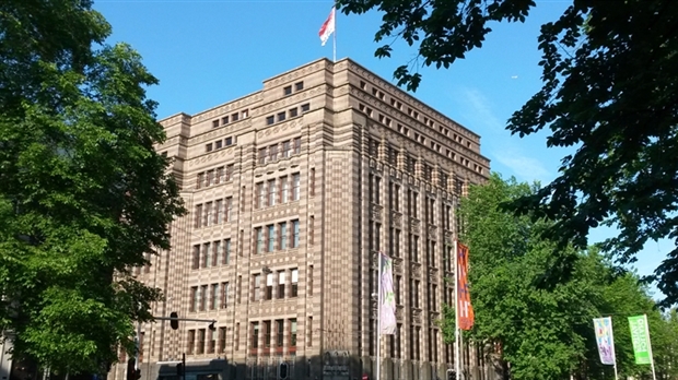 Budynek Stadsarchief Amsterdam z fasadą z czerwonej cegły, wieloma oknami i flagami, otoczony drzewami pod czystym błękitnym niebem