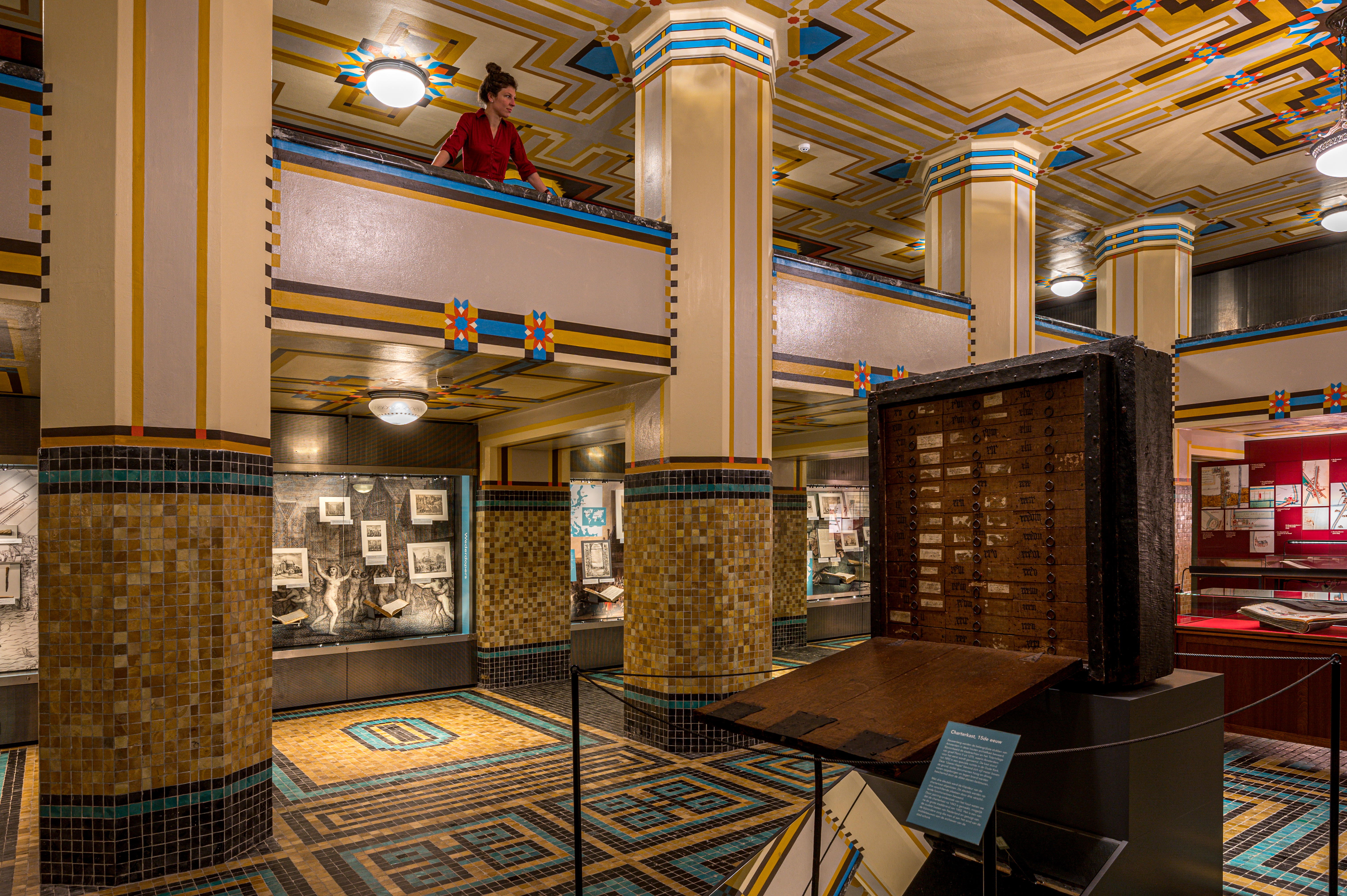 Wielkie wnętrze w stylu Art Deco Archiwum Miejskiego Amsterdamu z kafelkowymi kolumnami, geometrycznymi wzorami sufitu i wystawami