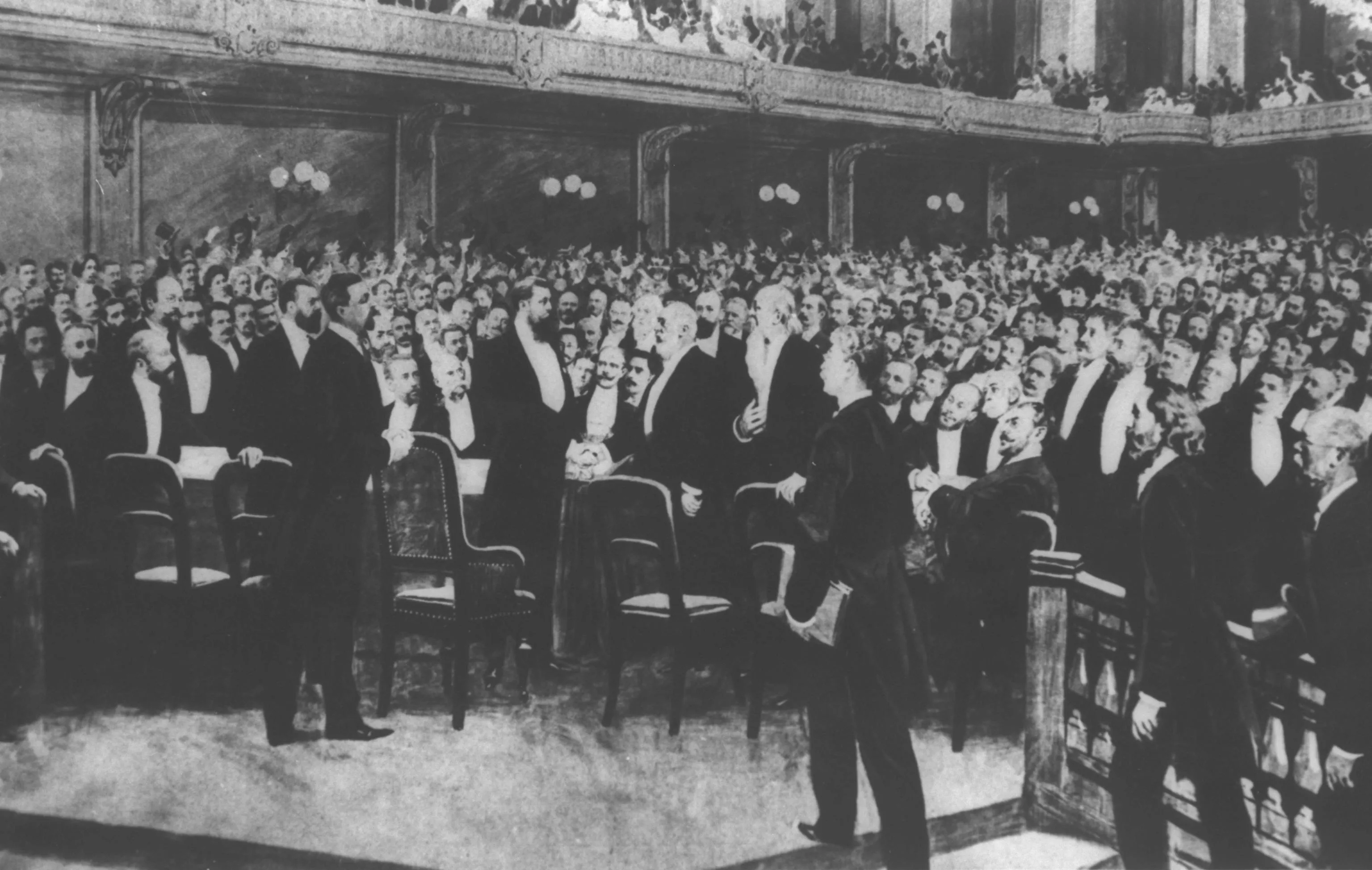 Black-and-white historical photograph of a large ornate concert hall filled with a dense crowd of men in formal attire, with figures standing in the foreground and balconies visible above