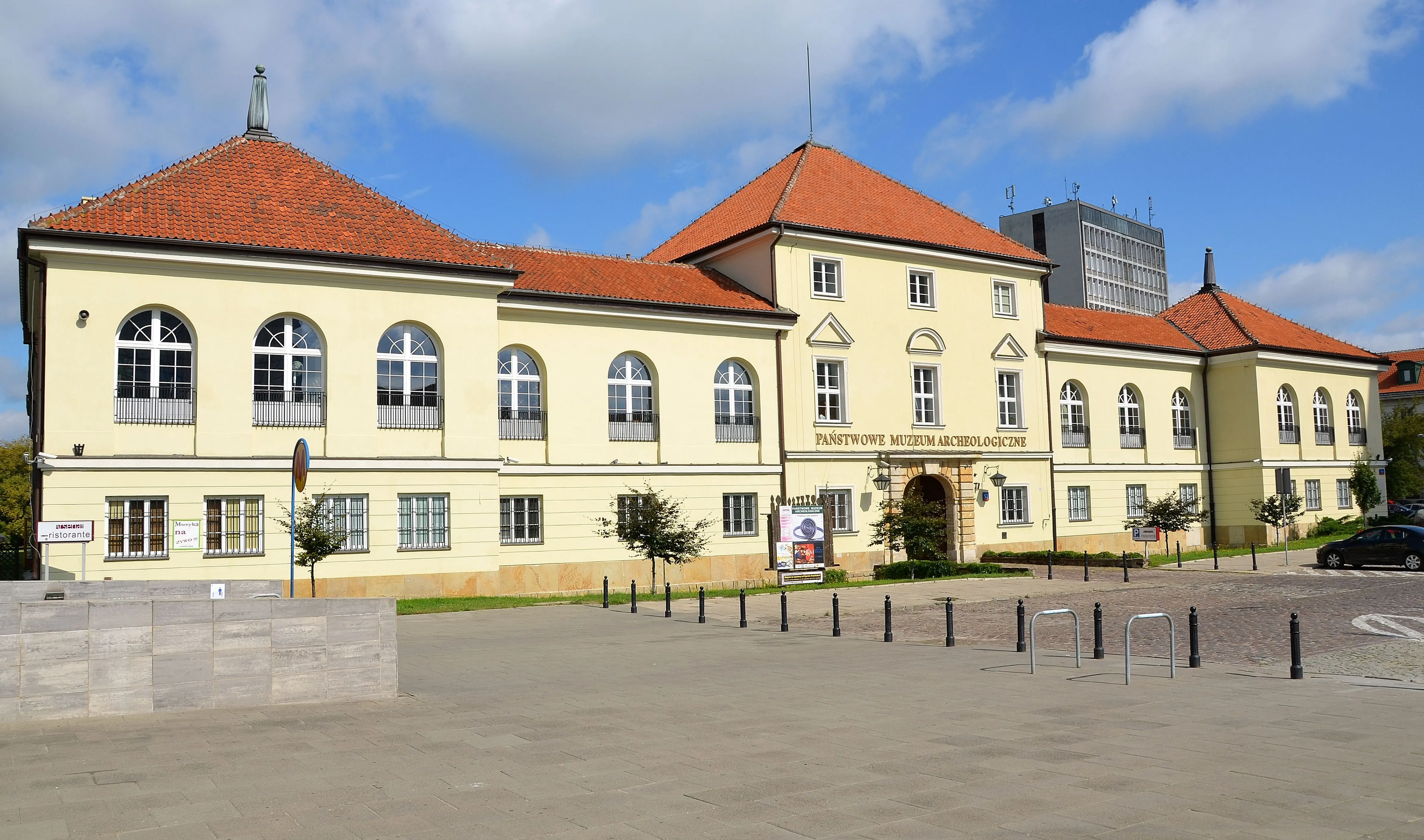 geel gebouw met rood pannendak en rondboogvensters, geïdentificeerd als het Nationaal Archeologisch Museum in Warschau