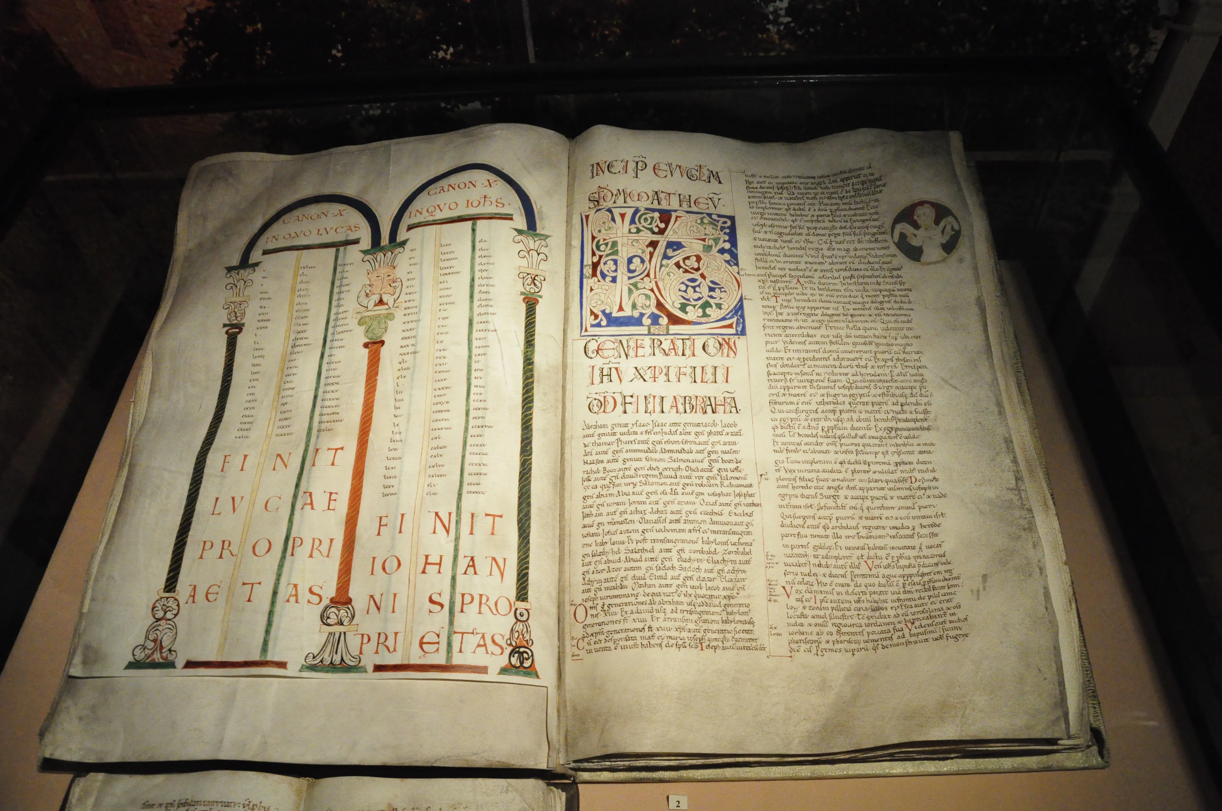 open verlicht manuscript met sierlijke belettering en illustraties in een vitrine