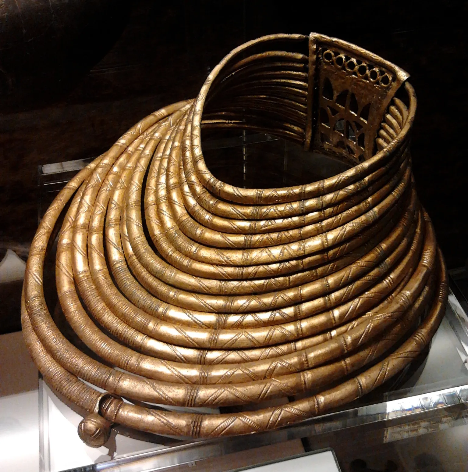 Een opgerolde bronzen borstplaat met ingewikkelde patronen, tentoongesteld in een vitrine in het museum