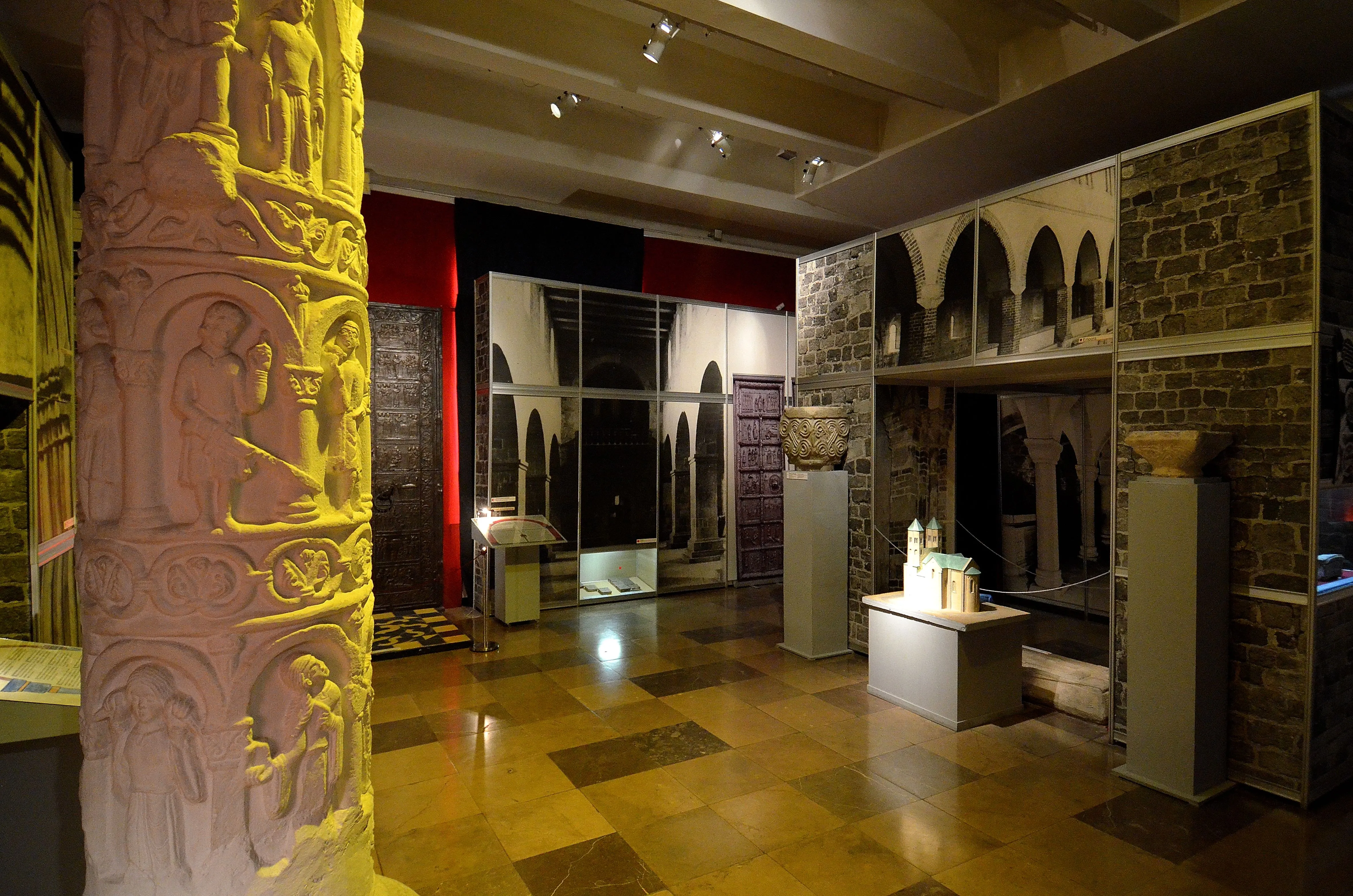 exhibitiezaal met gebeeldhouwde stenen zuil, vitrines en boogvormige architectonische elementen