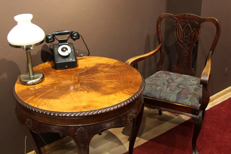A wooden table with a lamp and rotary phone next to a carved wooden chair