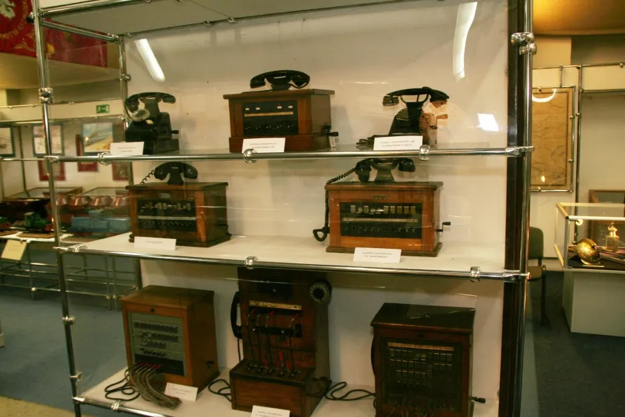 Glass display case with multiple vintage telephones and communication devices on shelves