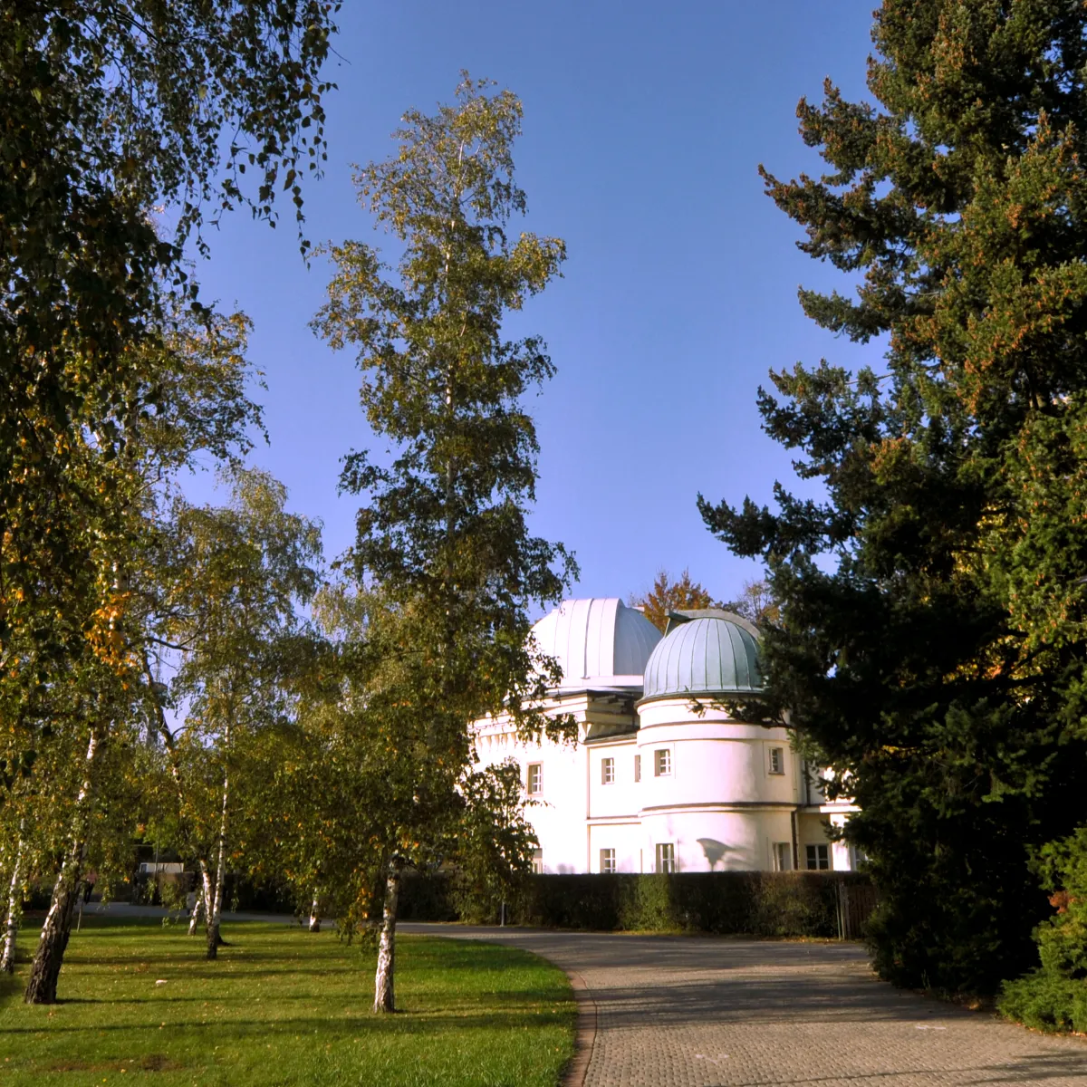 White observatory building with two domes surrounded by trees and green grass under a blue sky