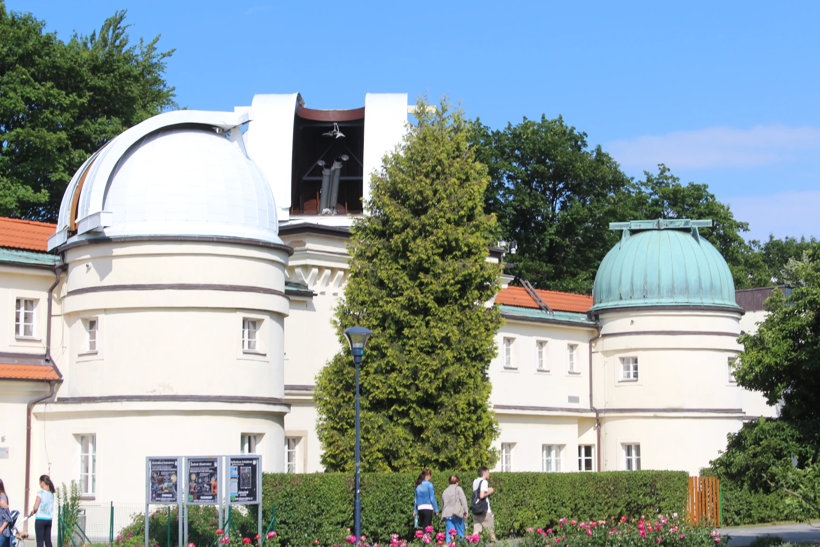 White observatory building with two domes, one white and one green, surrounded by trees and people in front.