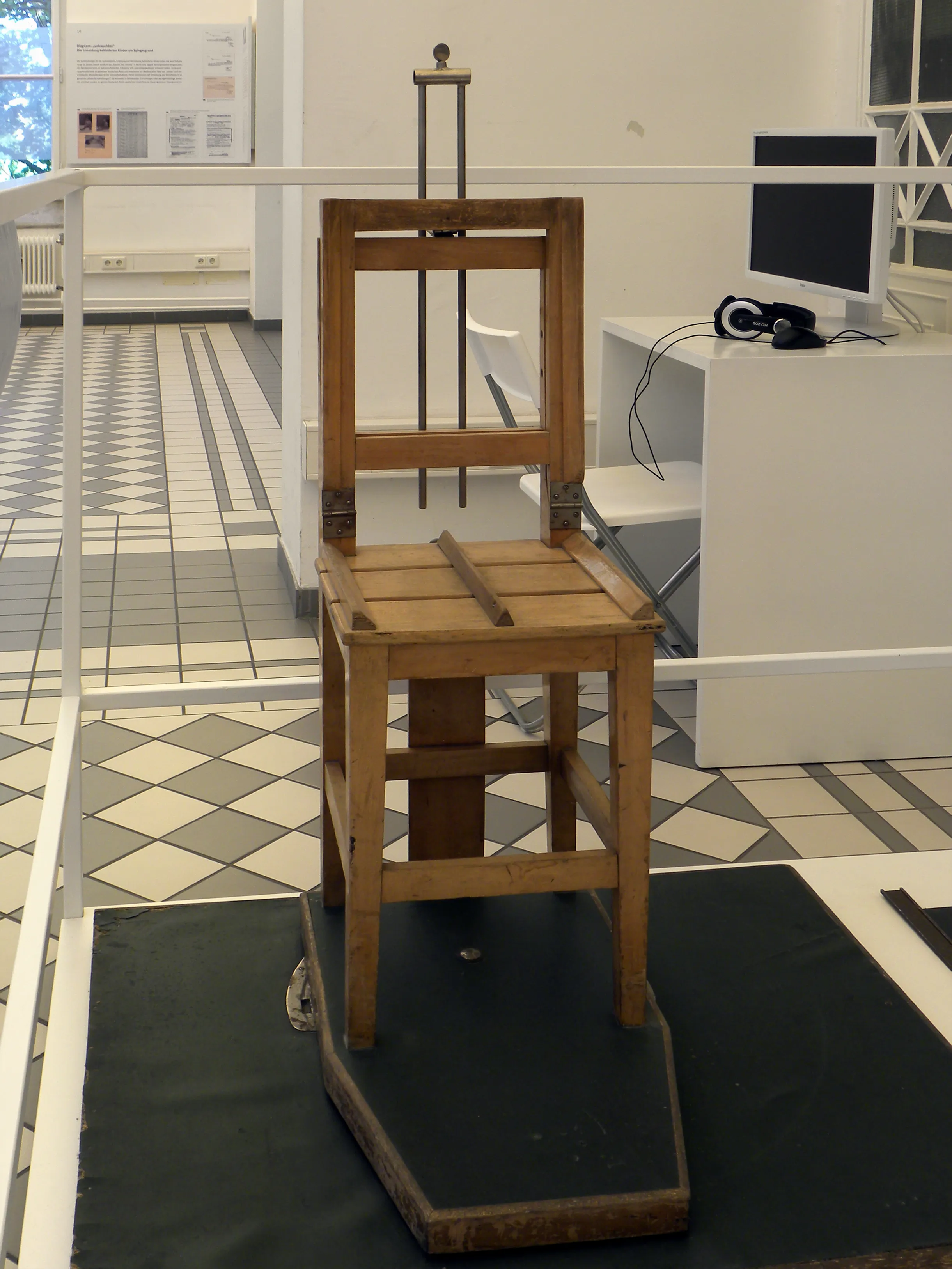 silla de sujeción de madera sobre una plataforma negra en una exposición de museo