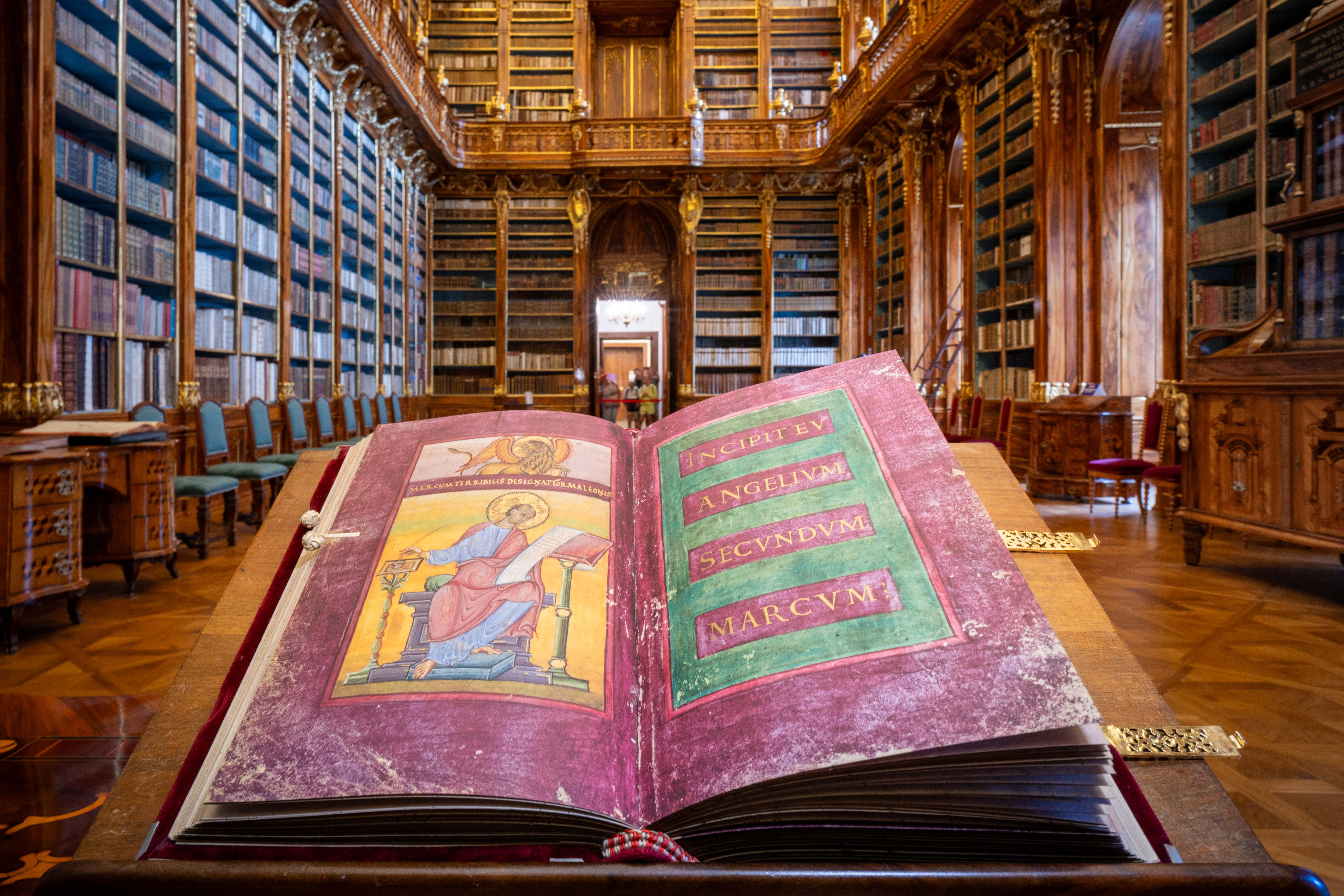 Otwarty iluminowany rękopis na stole w wielkiej bibliotece z wysokimi drewnianymi regałami i ozdobną architekturą