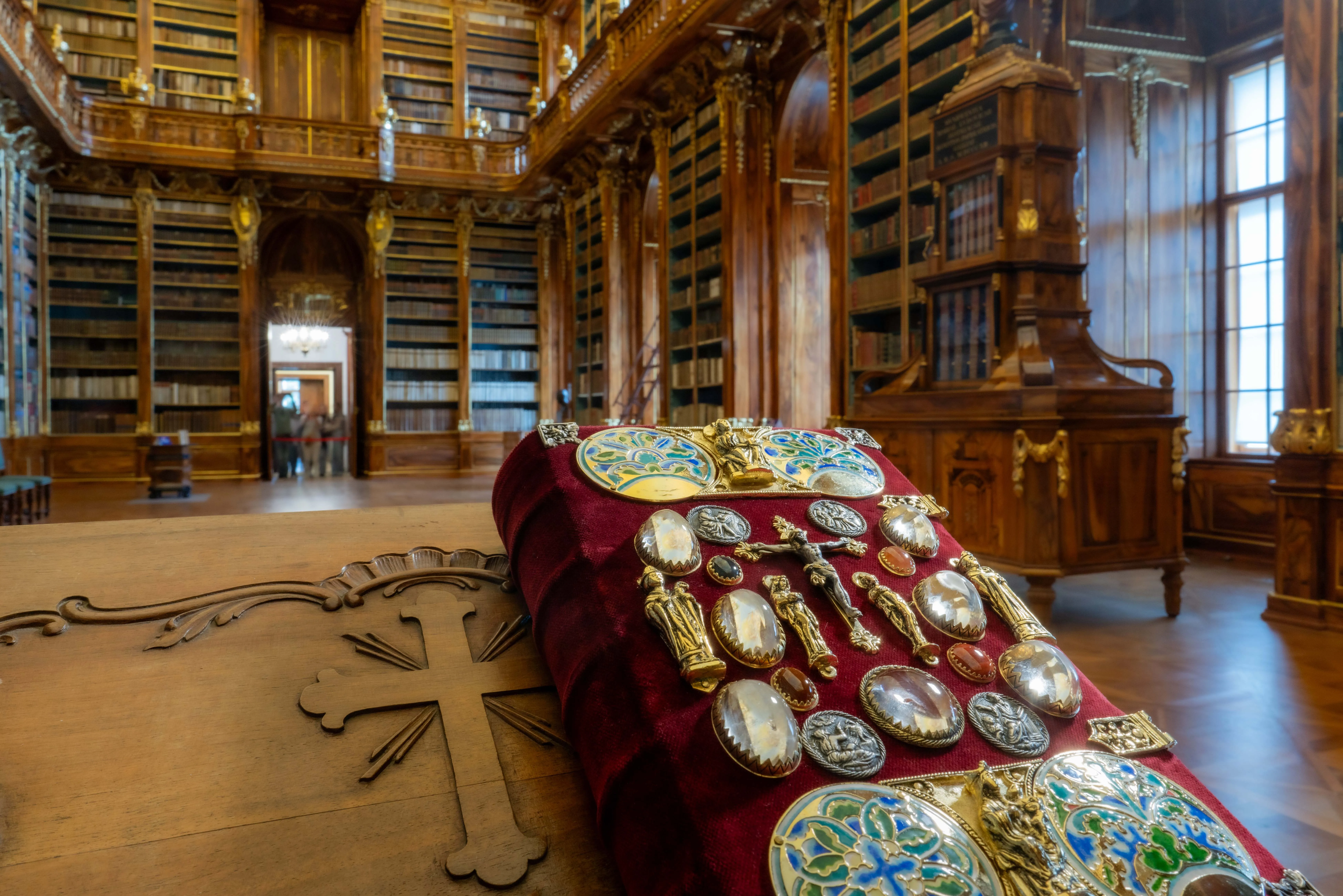 Ozdobne artefakty religijne wyłożone na czerwonej aksamitnej poduszce w wielkiej drewnianej bibliotece