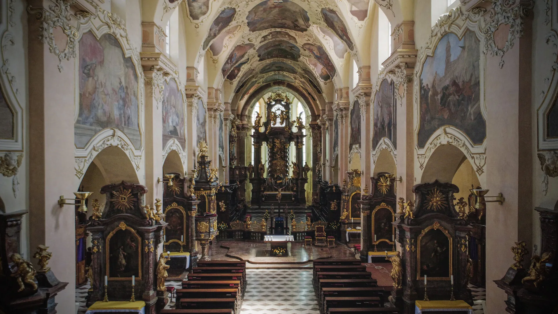 interior of a baroque church with ornate ceilings, gilded altars, and wooden pews