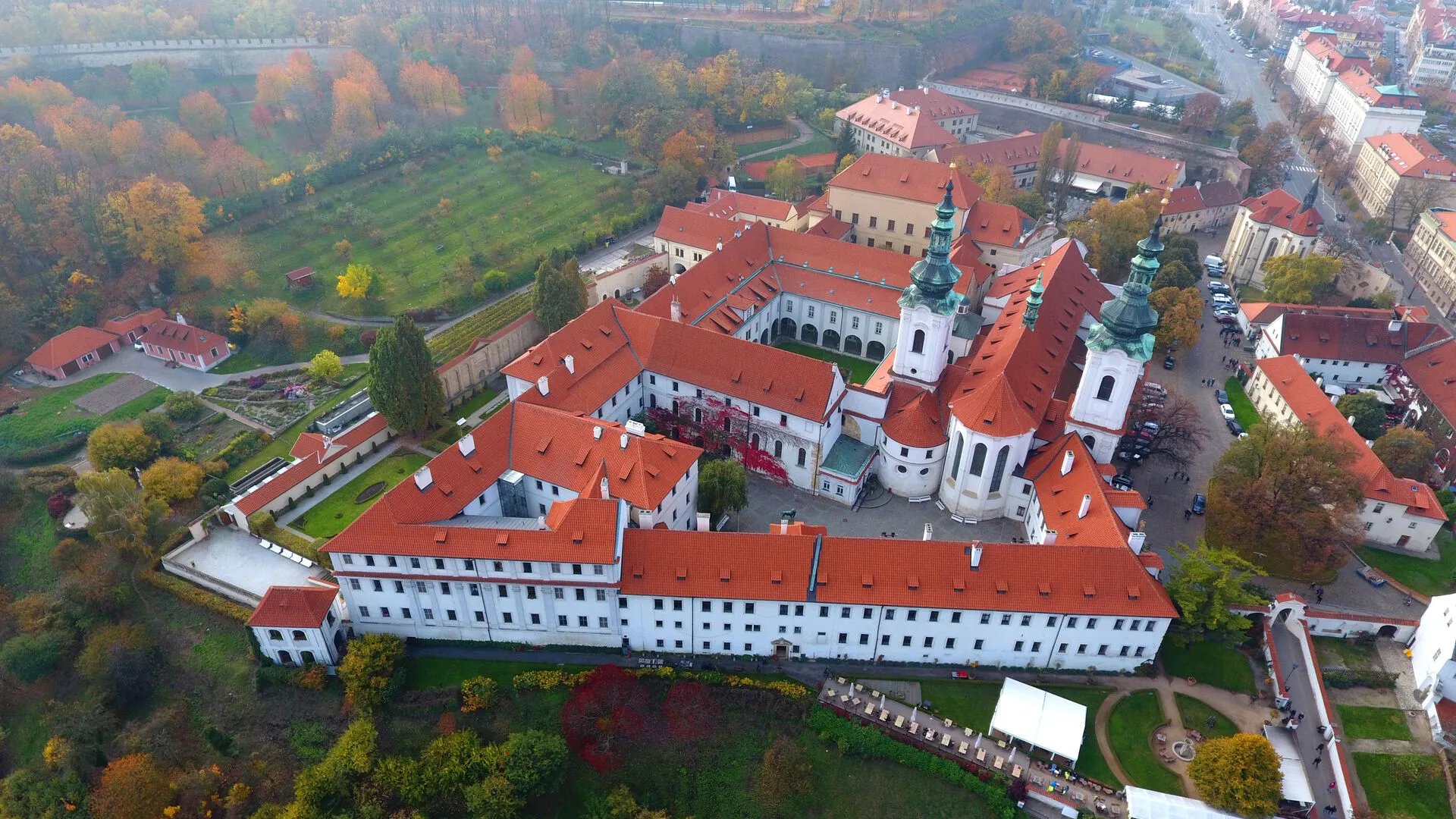 Widok z lotu ptaka na Klasztor na Strahovie z białymi budynkami, czerwonymi dachami i otaczającym zielonym krajobrazem.