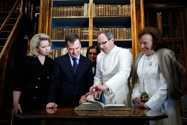 Four people standing around a table in a library with bookshelves in the background