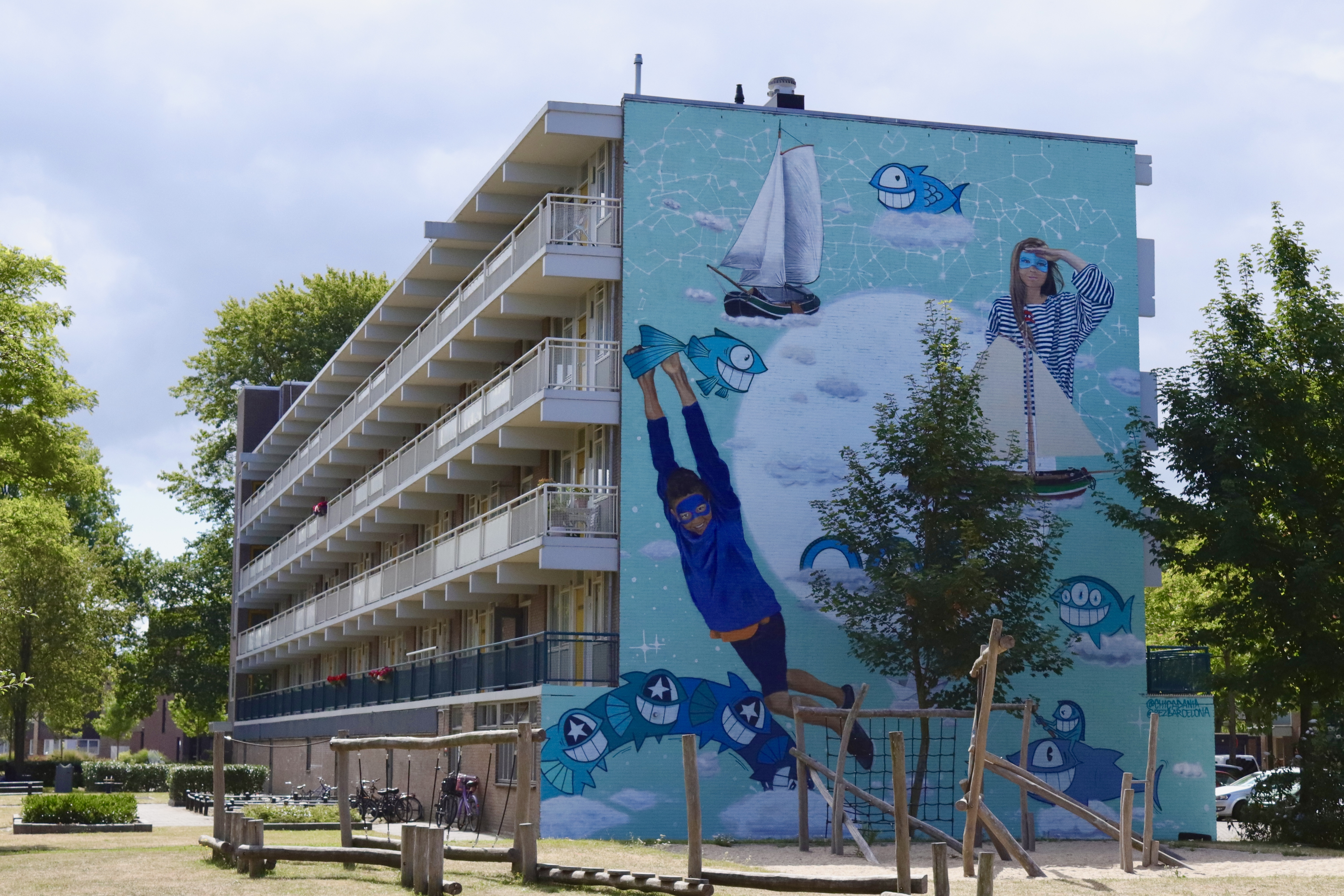Vibrant turquoise mural on a multi-story building featuring a figure hanging from a moon, sailboats, and blue sea creatures at Street Art Museum Amsterdam
