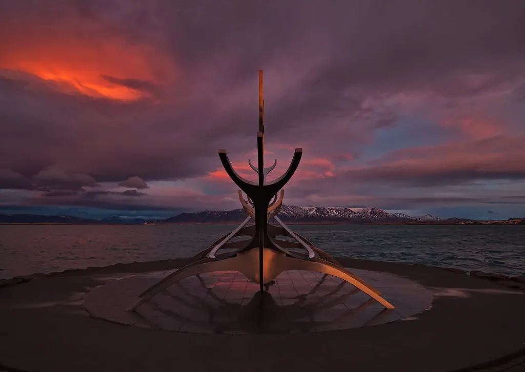 Rzeźba ze stali nierdzewnej Sun Voyager na tle dramatycznego fioletowo-pomarańczowego nieba o zachodzie słońca nad nabrzeżem Reykjavíku.