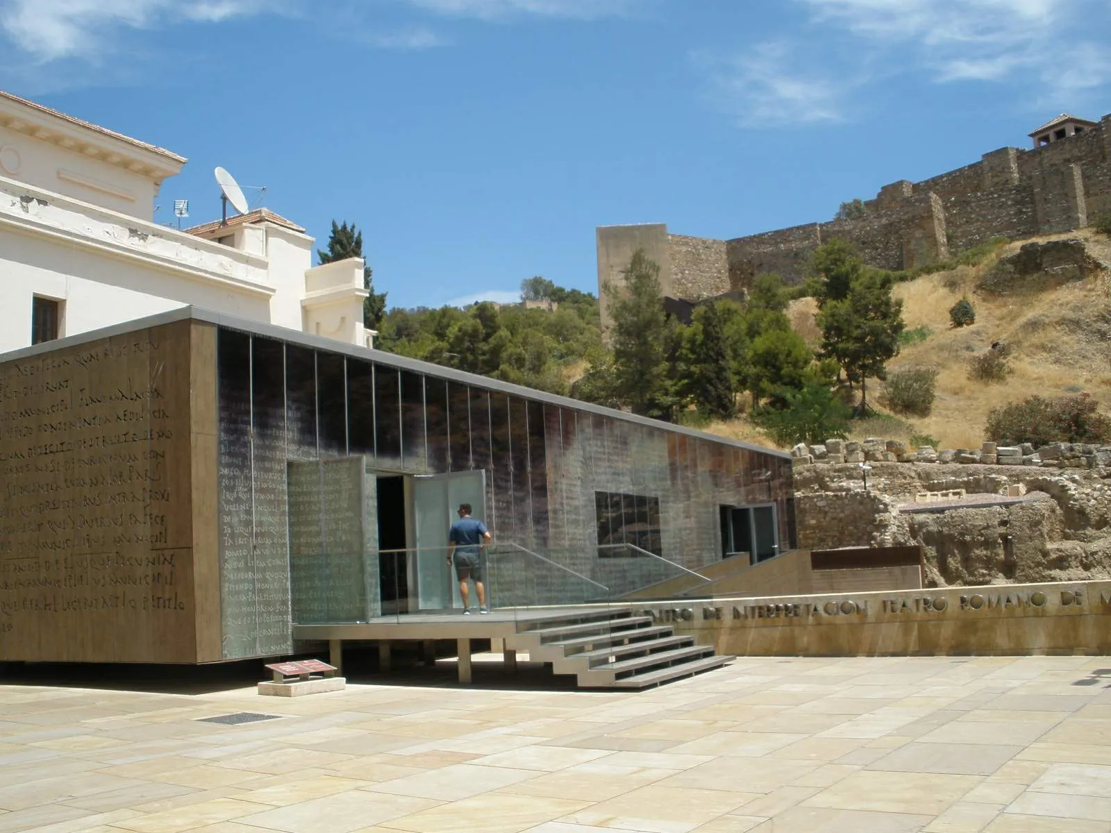 Moderno edificio del centro de interpretación, construido en cristal y piedra, junto al Teatro Romano de Málaga, con la fortaleza de la Alcazaba visible en la colina de atrás