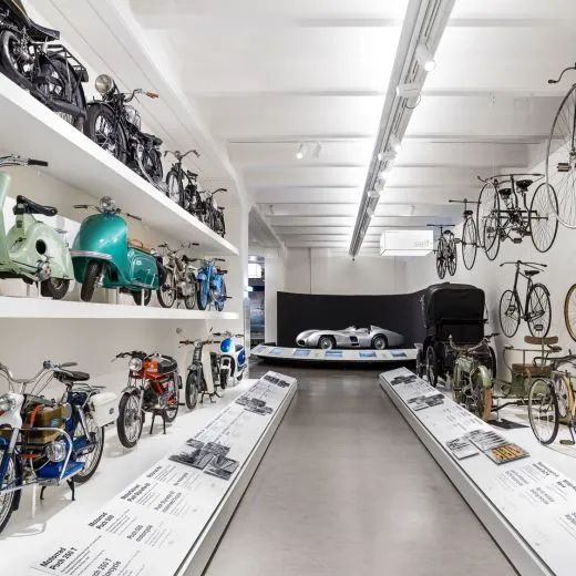 Sala de exposiciones con motocicletas, scooters y bicicletas vintage en estantes y paredes de exhibición