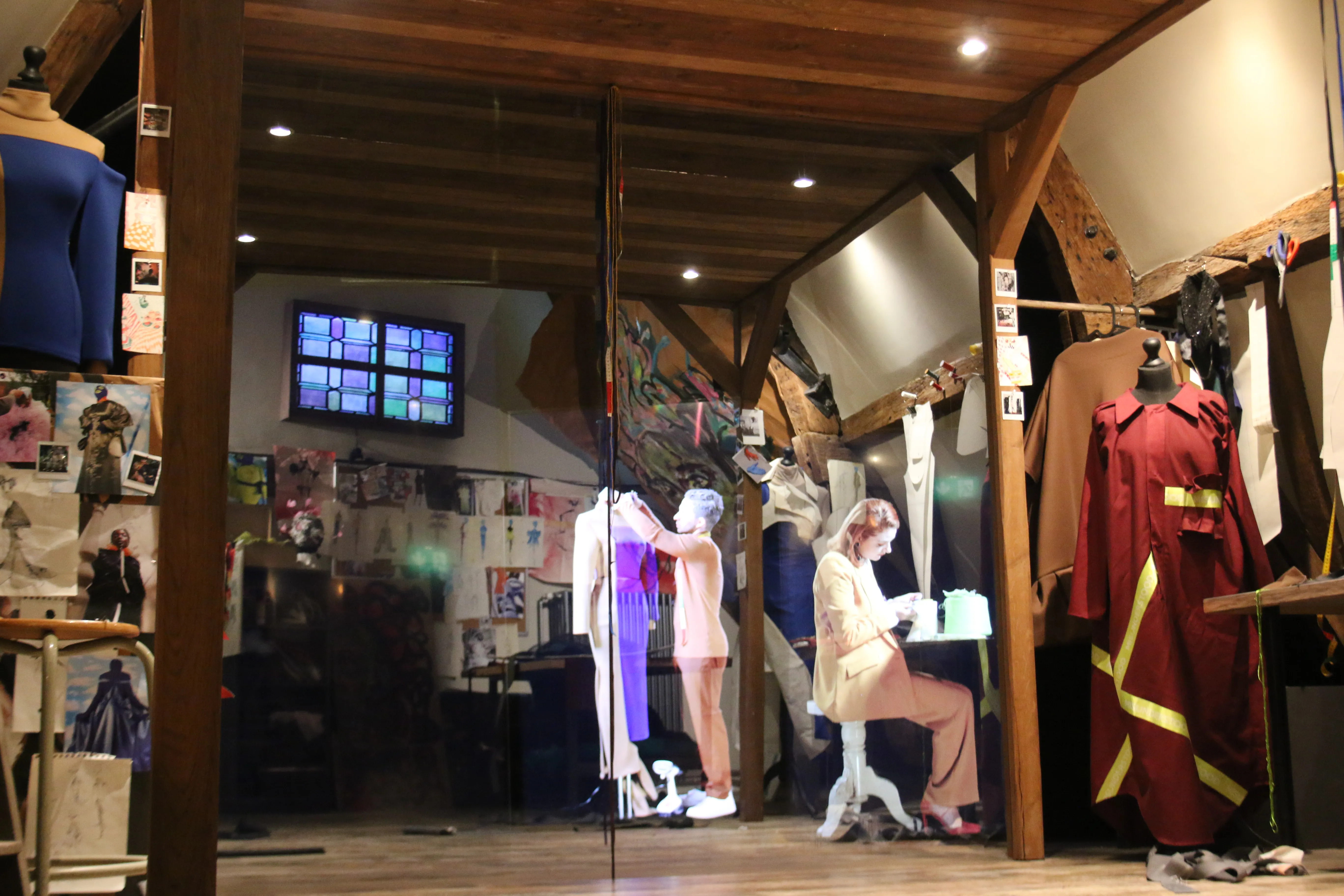 Sala de exposiciones con maniquíes vestidos con trajes que incluyen un uniforme de bombero, vigas de madera en el techo, una pantalla de televisión montada en la pared y paneles informativos.