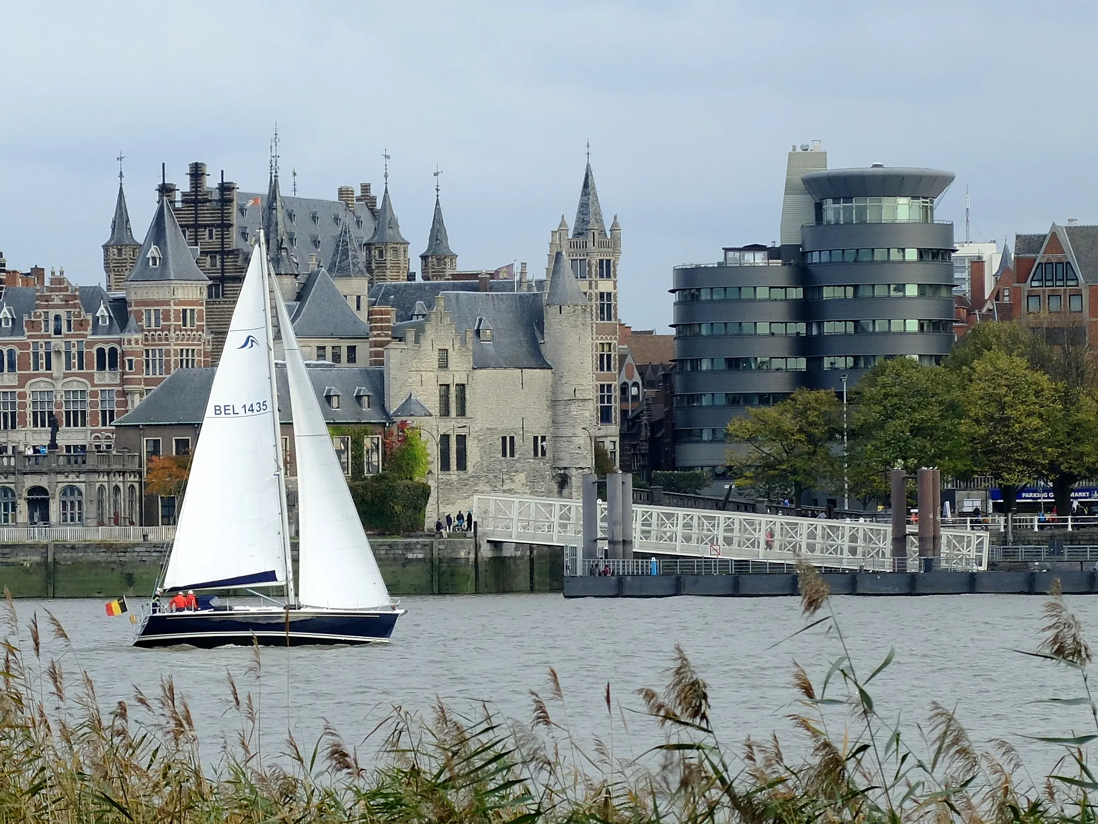 Histórico castillo Het Steen a orillas del río en Amberes, con un velero blanco en el agua y juncos en primer plano