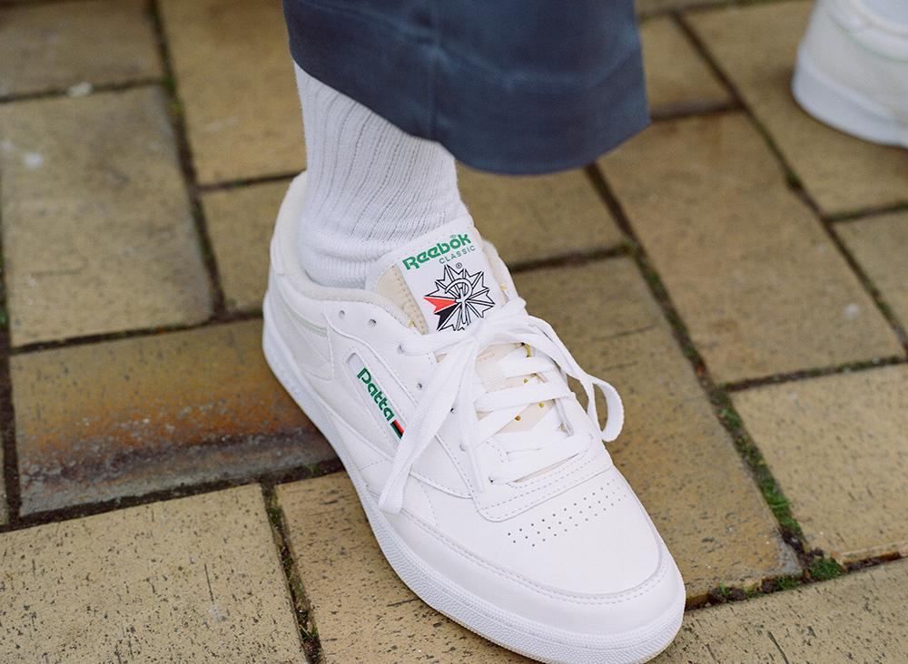Zapatilla blanca Reebok con marca Patta usada con calcetines blancos sobre pavimento de ladrillo