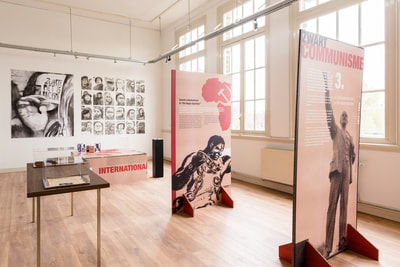 Espacio de exposición con grandes paneles de exhibición que incluyen imágenes históricas y texto, pisos de madera y ventanas altas en una sala de galería luminosa