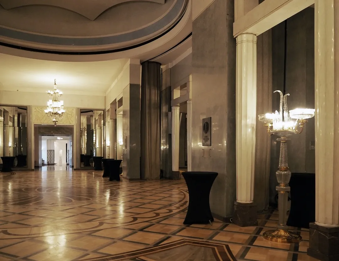 long hallway with ornate tiled floors, classical columns, and chandeliers
