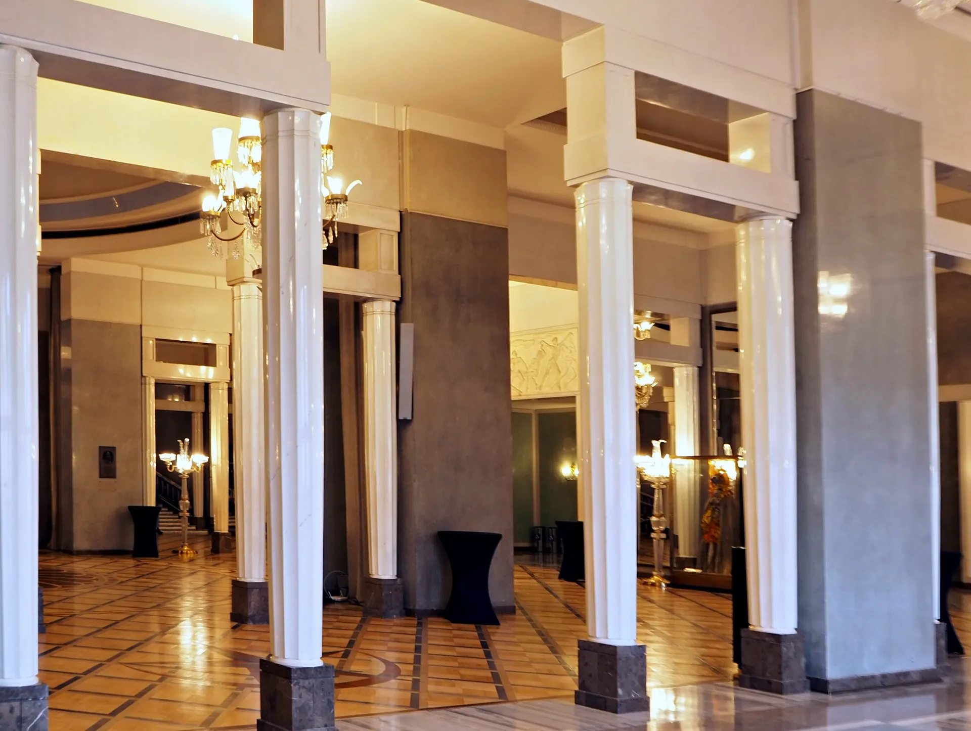 Grand hall with white columns, chandeliers, and tiled floor