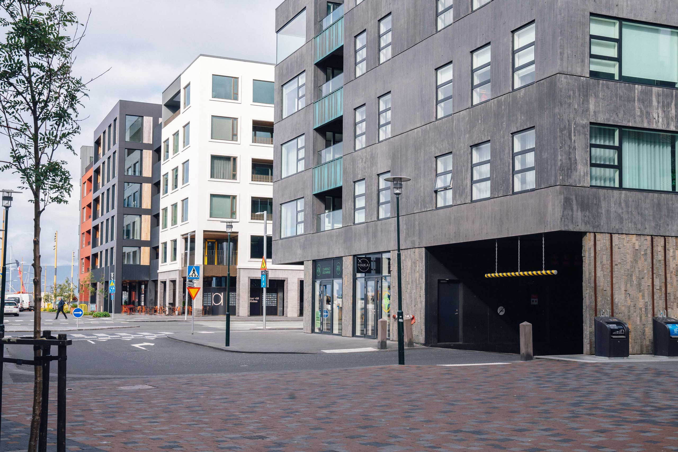 Street view of modern multi-story buildings with gray and white facades in the Hafnartorg district, featuring cobblestone pavement and a parking garage entrance