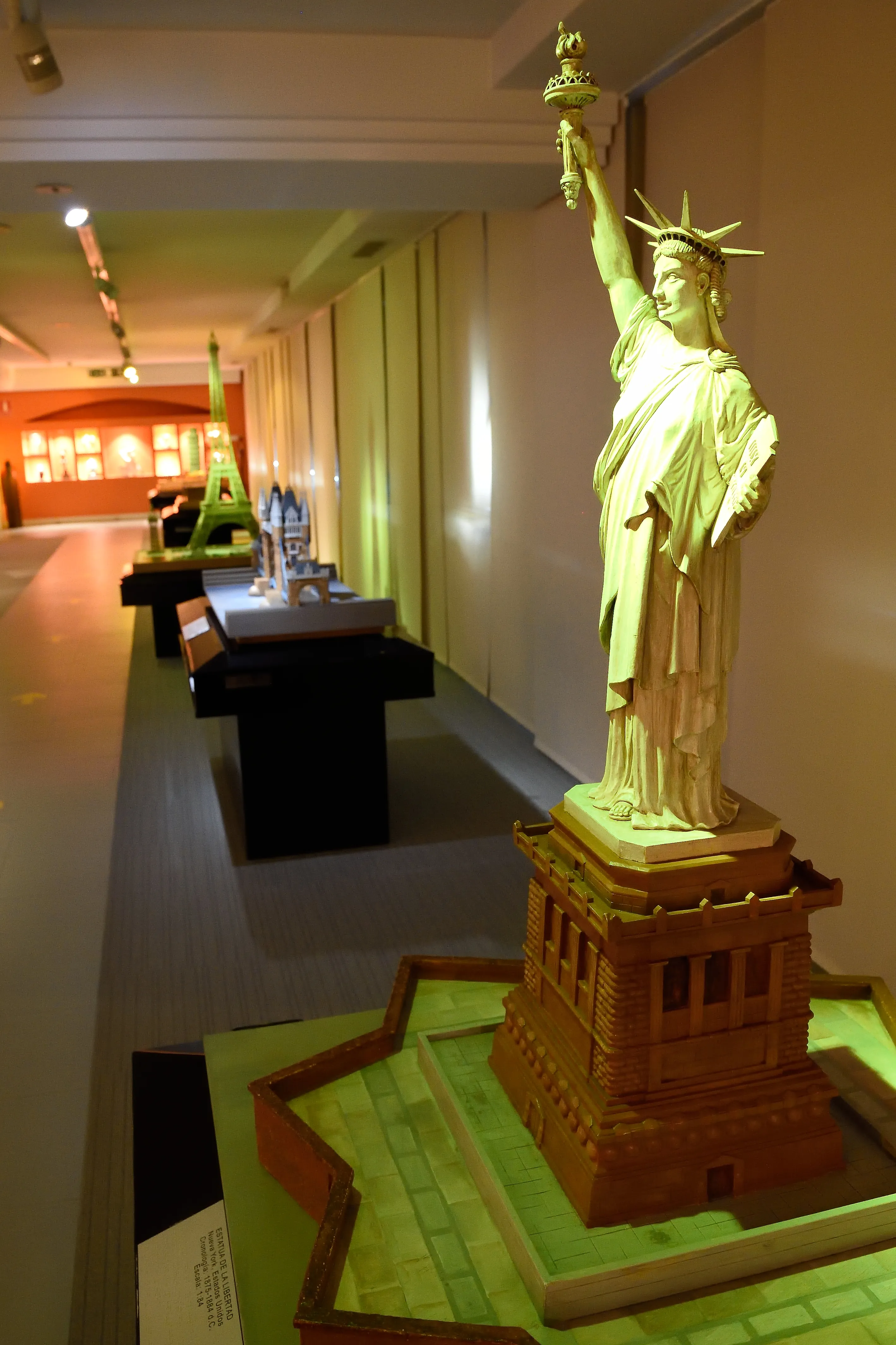 Modelo táctil de la Estatua de la Libertad sobre una base de madera en una sala de museo con otros modelos al fondo