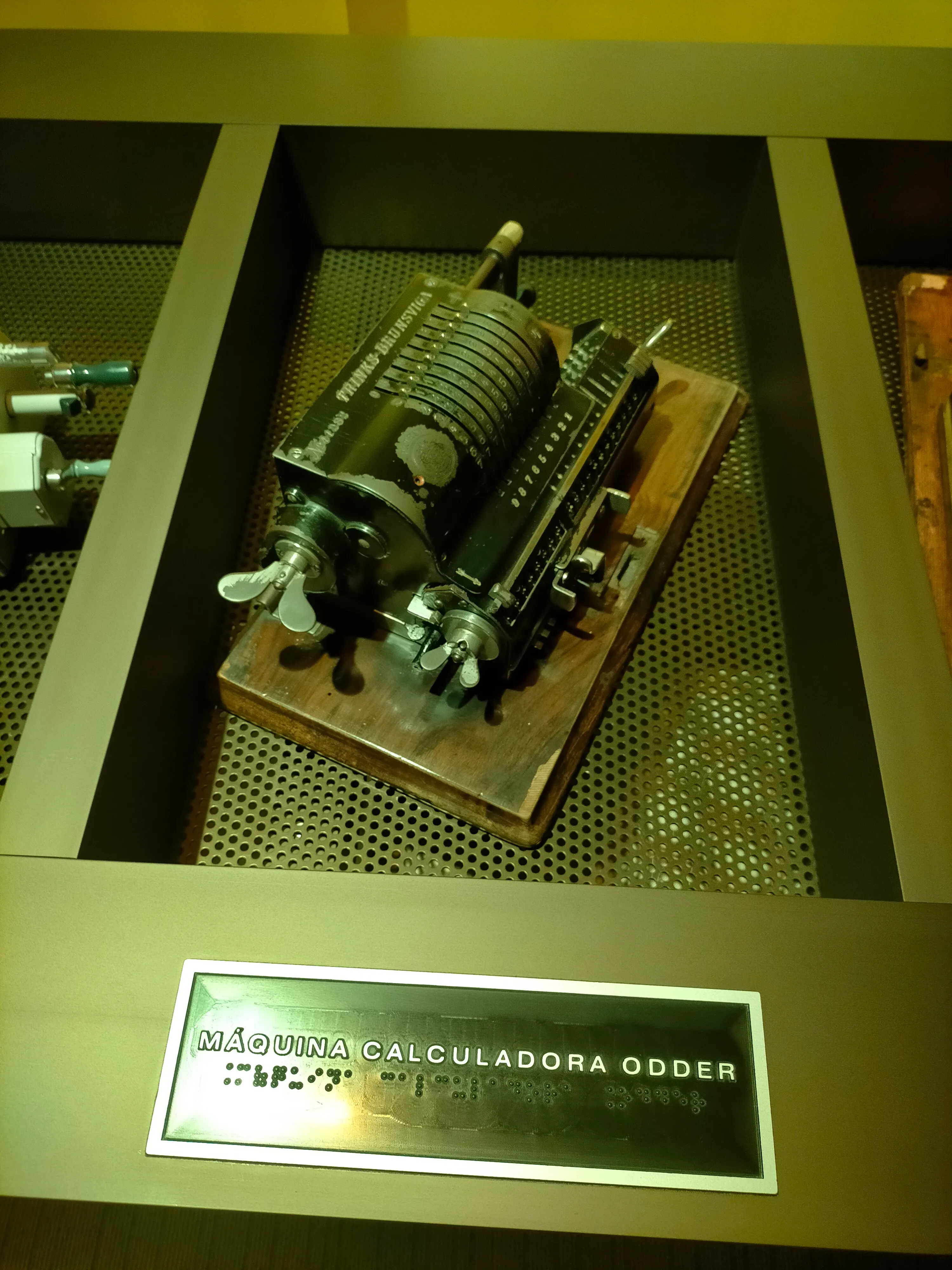 Exhibición táctil de una calculadora Odder vintage sobre una base de madera con una etiqueta en braille y español debajo