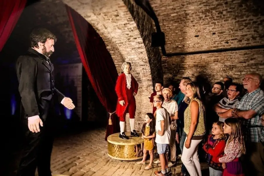 Figury animatroniczne muzyków w strojach historycznych stoją na scenie, a tłum zwiedzających obserwuje w kamiennej sali