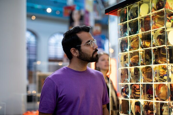 Una persona con una camisa morada observa una cuadrícula de vitrinas iluminadas que contienen artefactos históricos en el interior de un museo.