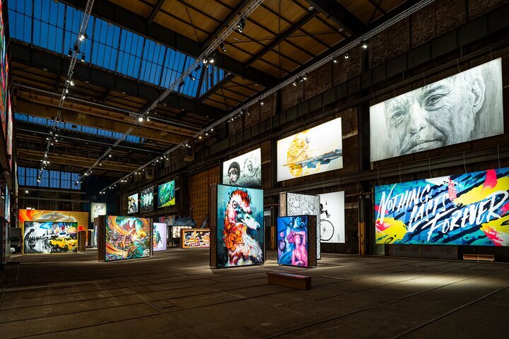 Espacioso interior industrial con coloridas obras de arte contemporáneas en paneles independientes bajo vigas expuestas y luces de riel