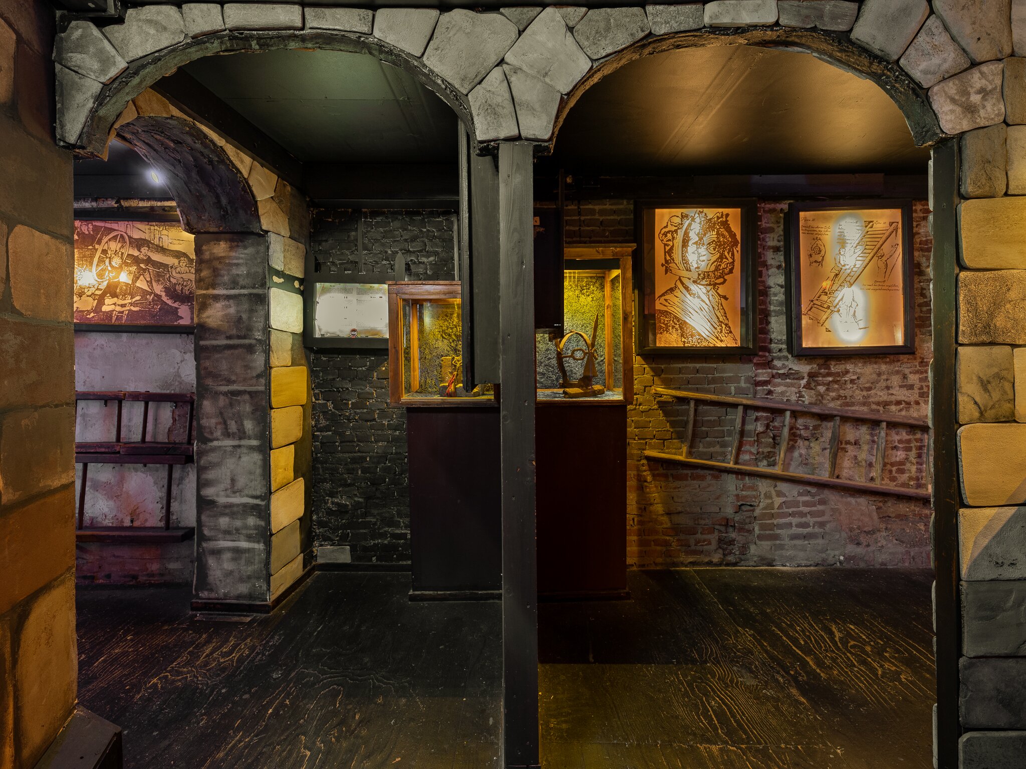 Arcos de piedra y muros de ladrillo en el interior tenuemente iluminado del Museo de la Tortura de Ámsterdam, con vitrinas iluminadas que exhiben artefactos históricos