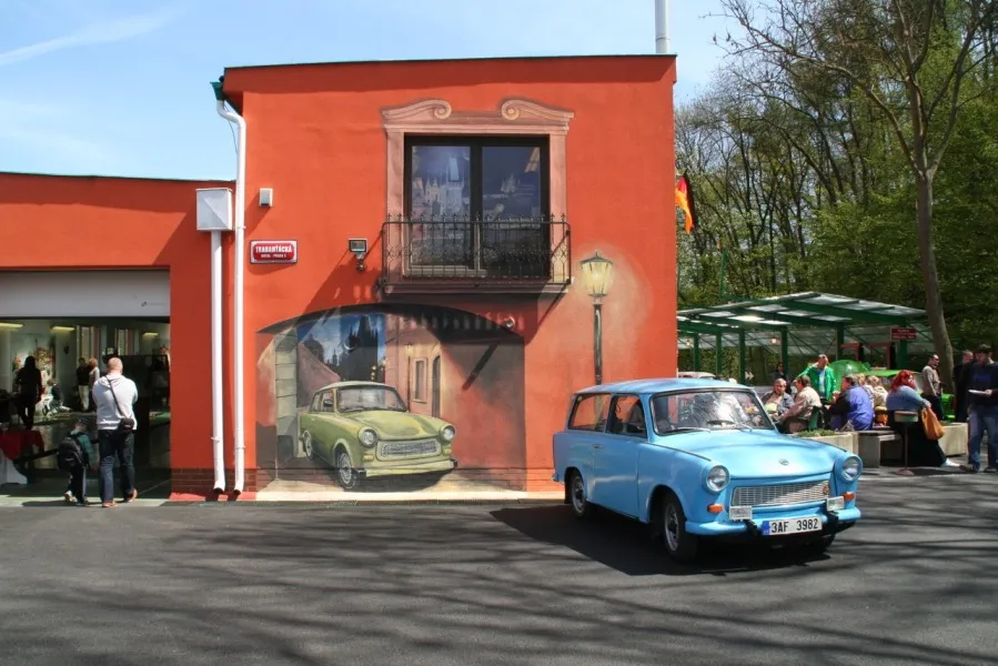 Niebieski samochód Trabant zaparkowany przed czerwonym budynkiem z muralem zielonego Trabanta na ścianie