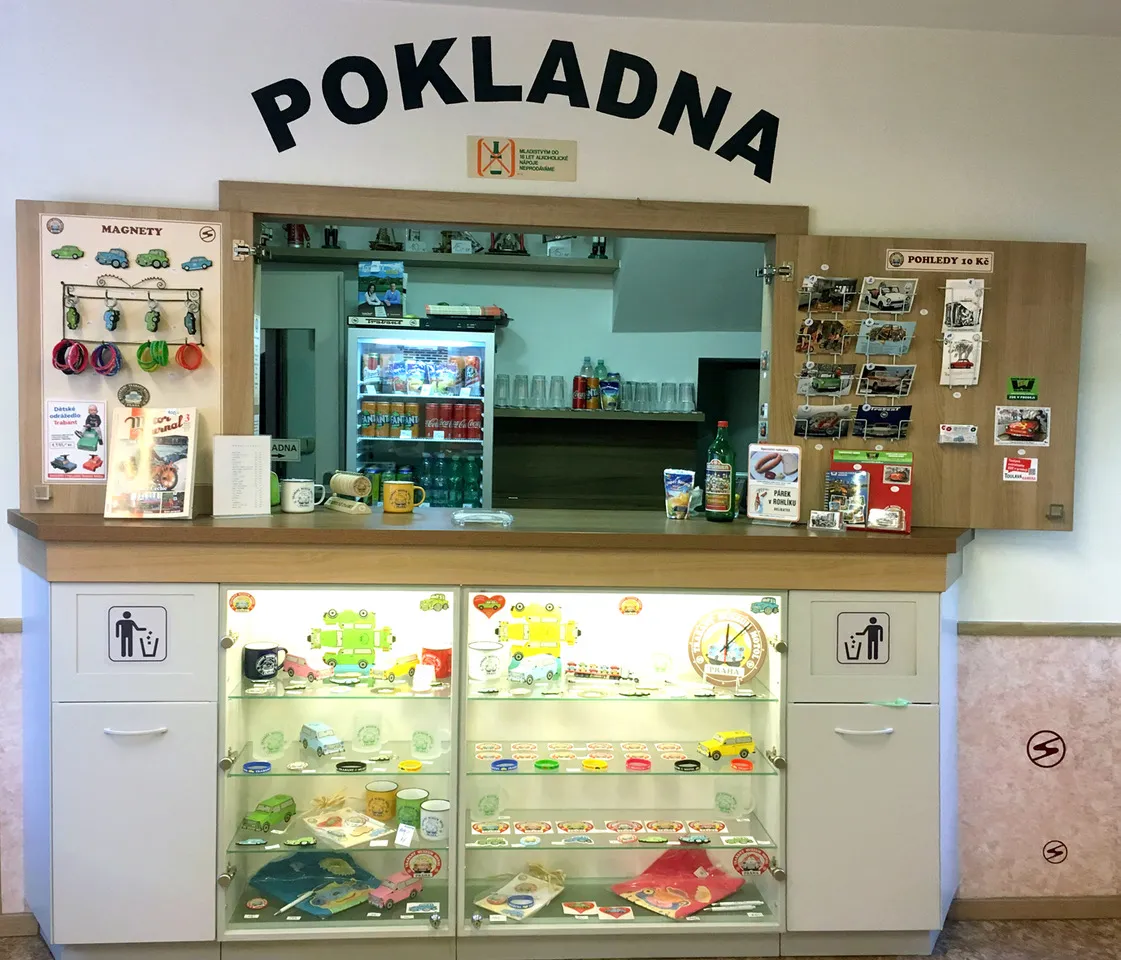 Widok wnętrza lady recepcyjnej w muzeum ze znakiem 'POKLADNA' i witrynami wypełnionymi pamiątkami