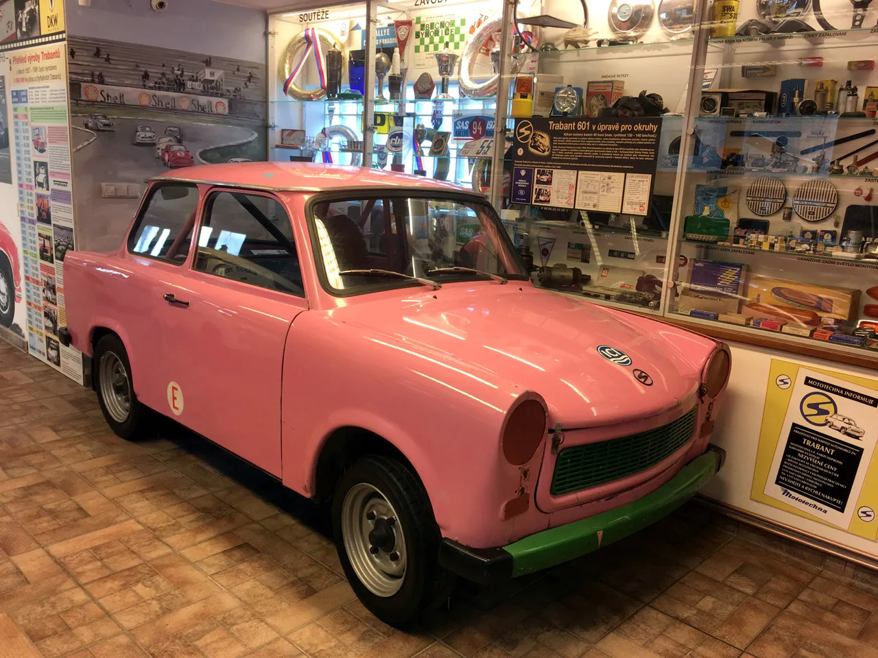 Różowy samochód Trabant na wystawie w muzeum ze szklanymi gablotami z pamiątkami w tle
