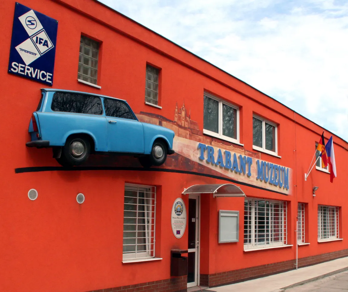 Pomarańczowy budynek z niebieskim samochodem Trabant zamontowanym z boku i napisem 'Trabant Muzeum'