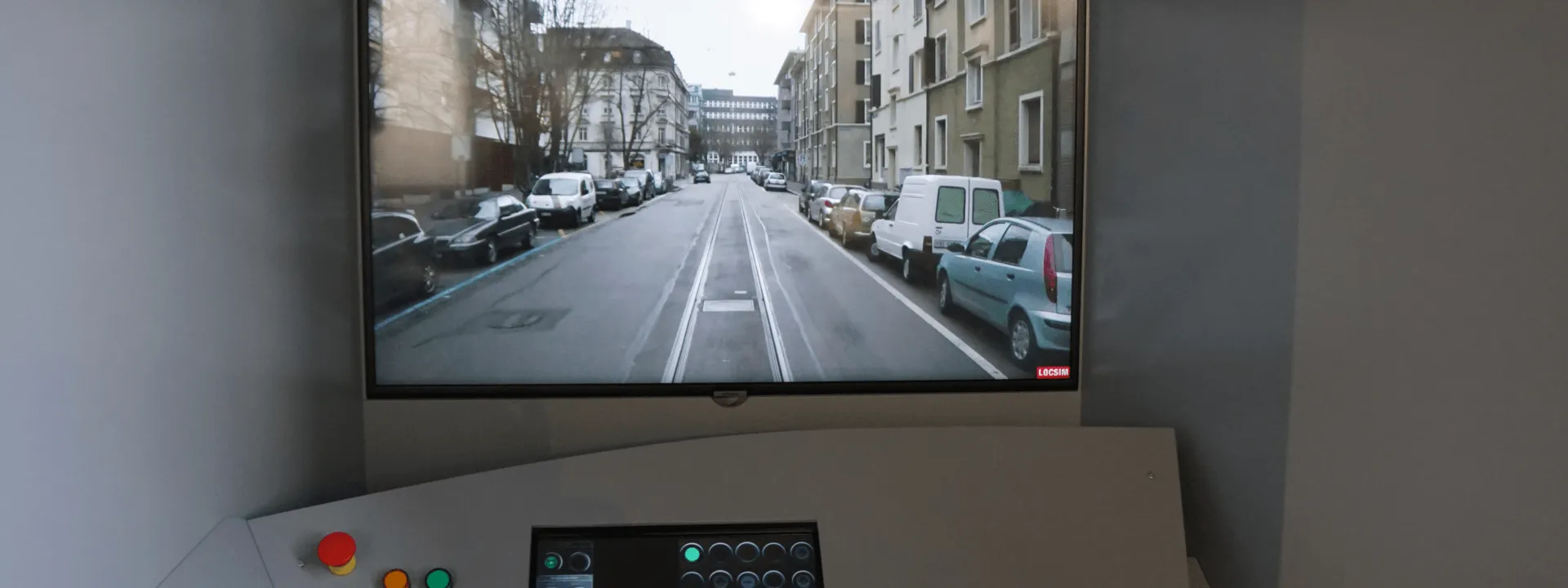 A tram driving simulator exhibit with a monitor showing a street view with tram tracks and a control panel with colored buttons and a small digital display below.