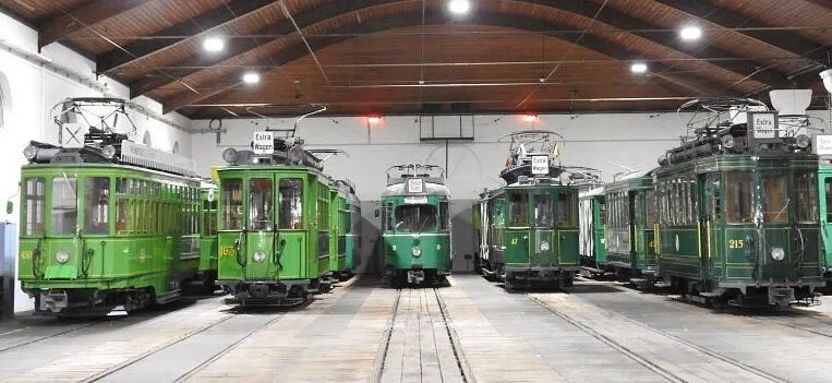 Interior of tram museum hall with multiple vintage green trams parked on parallel tracks under a wooden ceiling with overhead lights