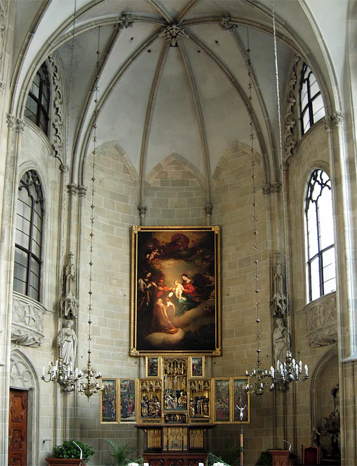 Interieur van een stenen kerk met een gewelfd plafond, grote ramen en een centraal schilderij boven een altaar.