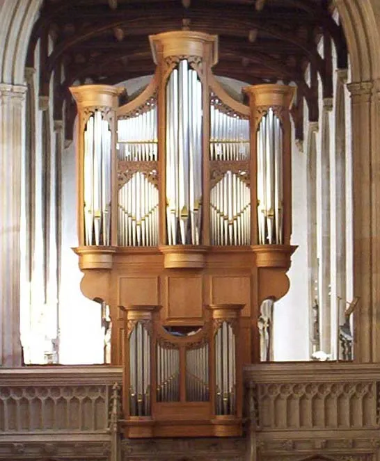 Gran órgano de tubos de madera con tubos de plata situado entre arcos góticos de piedra y bajo un techo de madera en el interior de una iglesia.