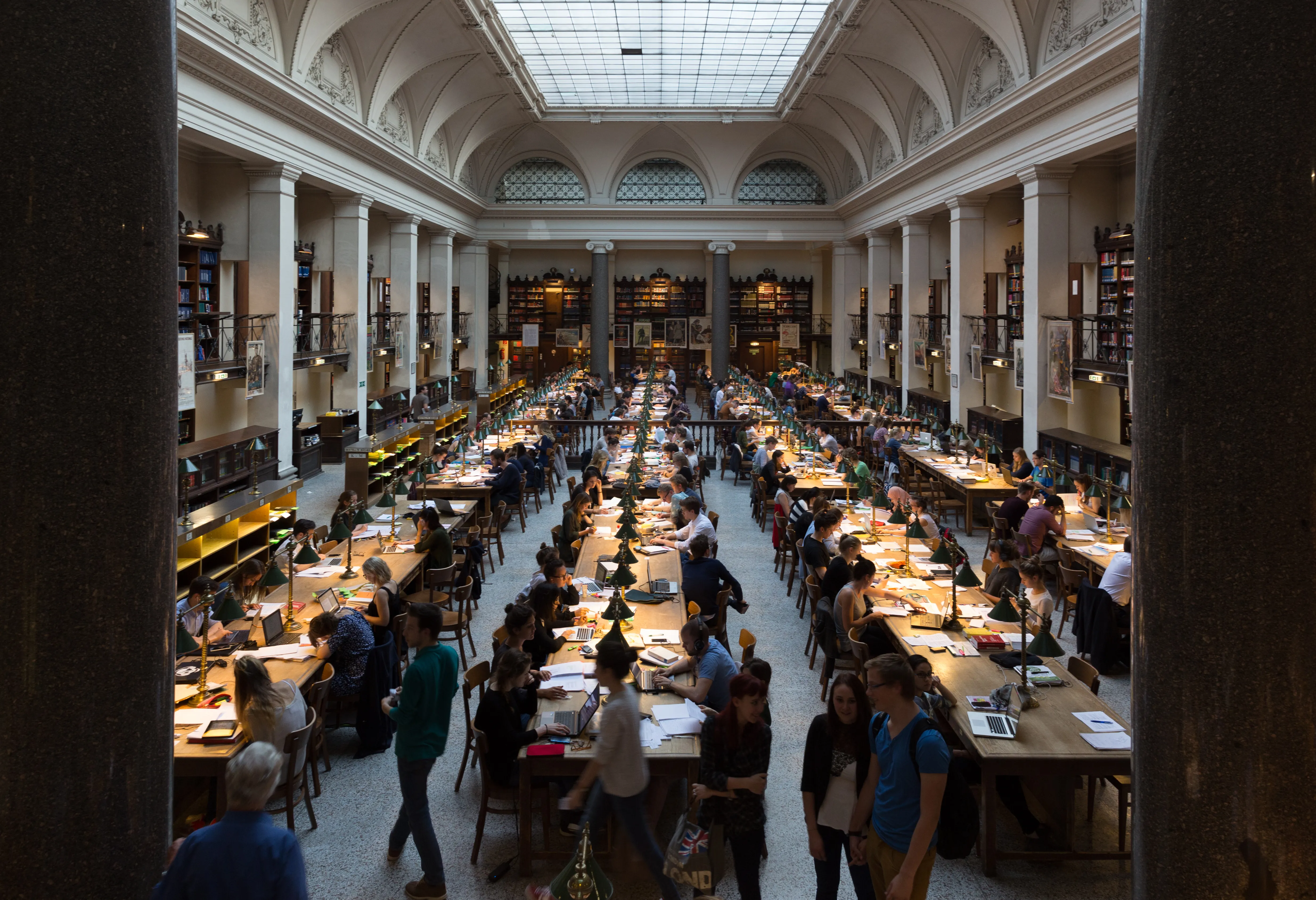 Gran sala de lectura con techos altos abovedados, columnas y hileras de mesas con gente estudiando