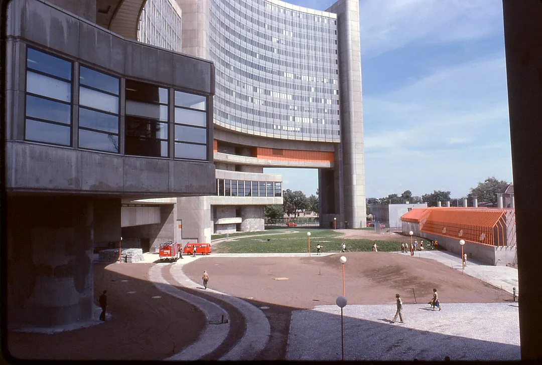 Modern gebouwencomplex met een gebogen glas toren en betonnen structuren onder een blauwe lucht