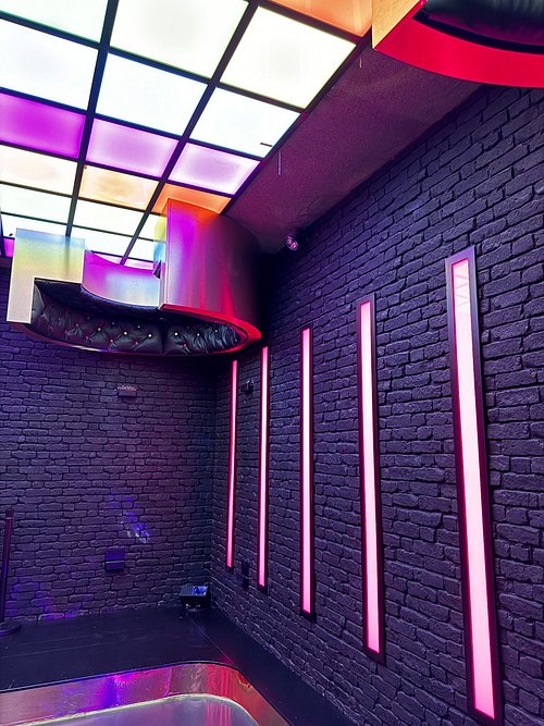 Brick-walled room with vertical pink neon lights, colorful grid ceiling, and metallic structure in an immersive attraction