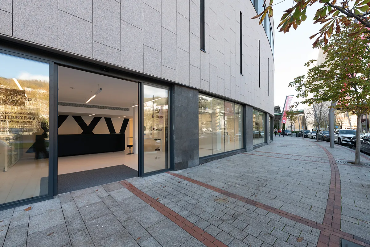 Fachada de un edificio moderno con grandes puertas de entrada de cristal y ventanales con la señalización URIBITARTE40 y BILBOARTE, junto a una acera pavimentada y árboles en la calle.