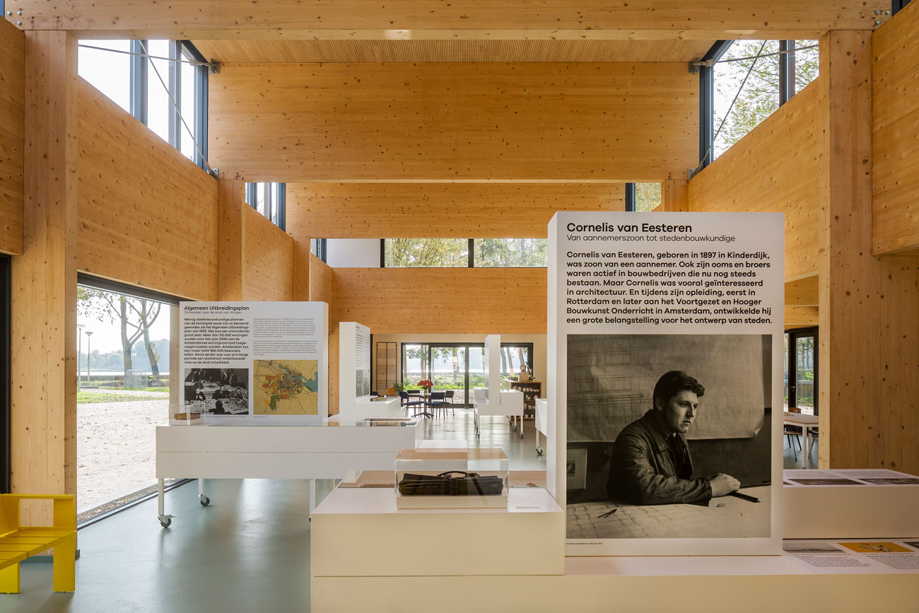 Moderne houten interieur met tentoonstellingspanelen, grote ramen en een display met tekst en een portret van Cornelis van Eesteren.